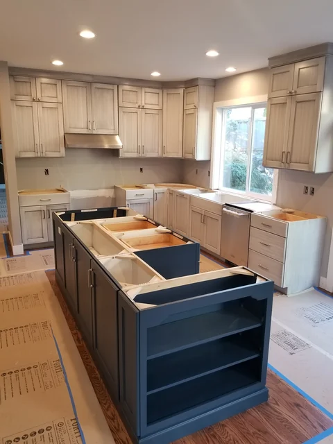 Two-tone kitchen cabinet installation in progress with dark island and light perimeter cabinets