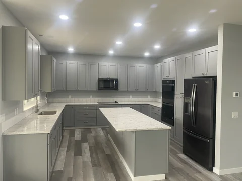 Finished gray shaker kitchen cabinetry with center island and light stone countertops